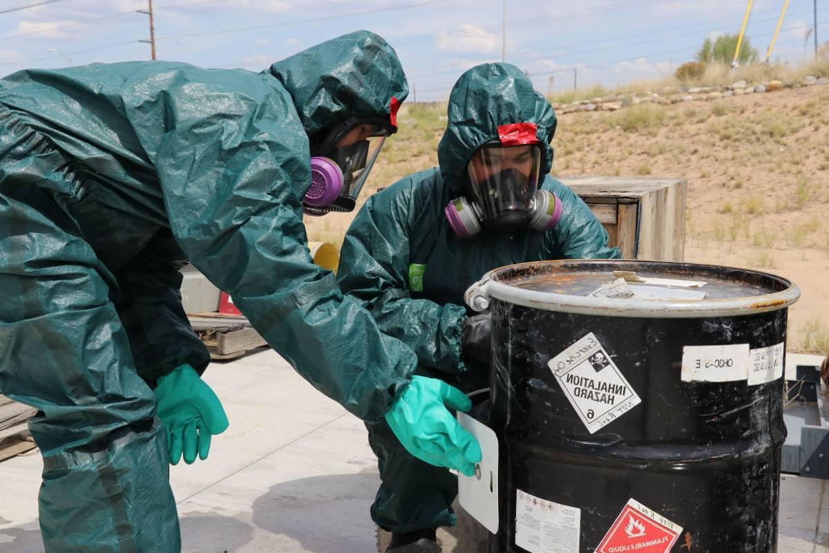 Two people, dressed in hazmat suits handle hazardous waste material.